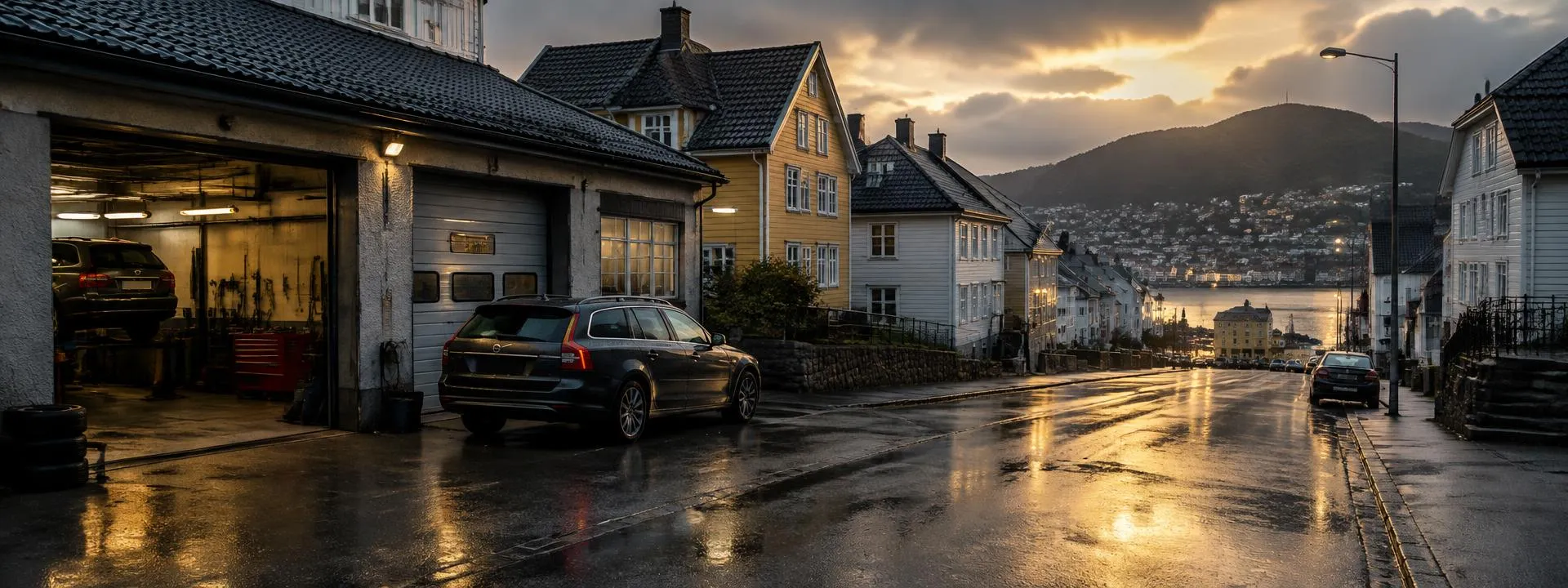 Våt gate i kveldslys med et bilverksted og trehus